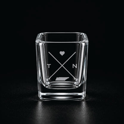 Engraved Tennessee shot glass with modern crossed-line state design and frosted laser engraving on a dark background.