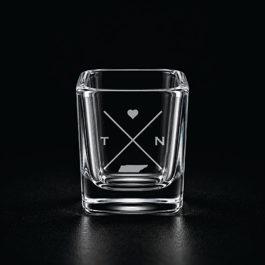 Engraved Tennessee shot glass with modern crossed-line state design and frosted laser engraving on a dark background.
