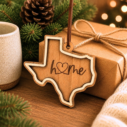 Wooden Texas-shaped ornament with 'home' engraving on a wrapped gift with pine cones and lights in the background.