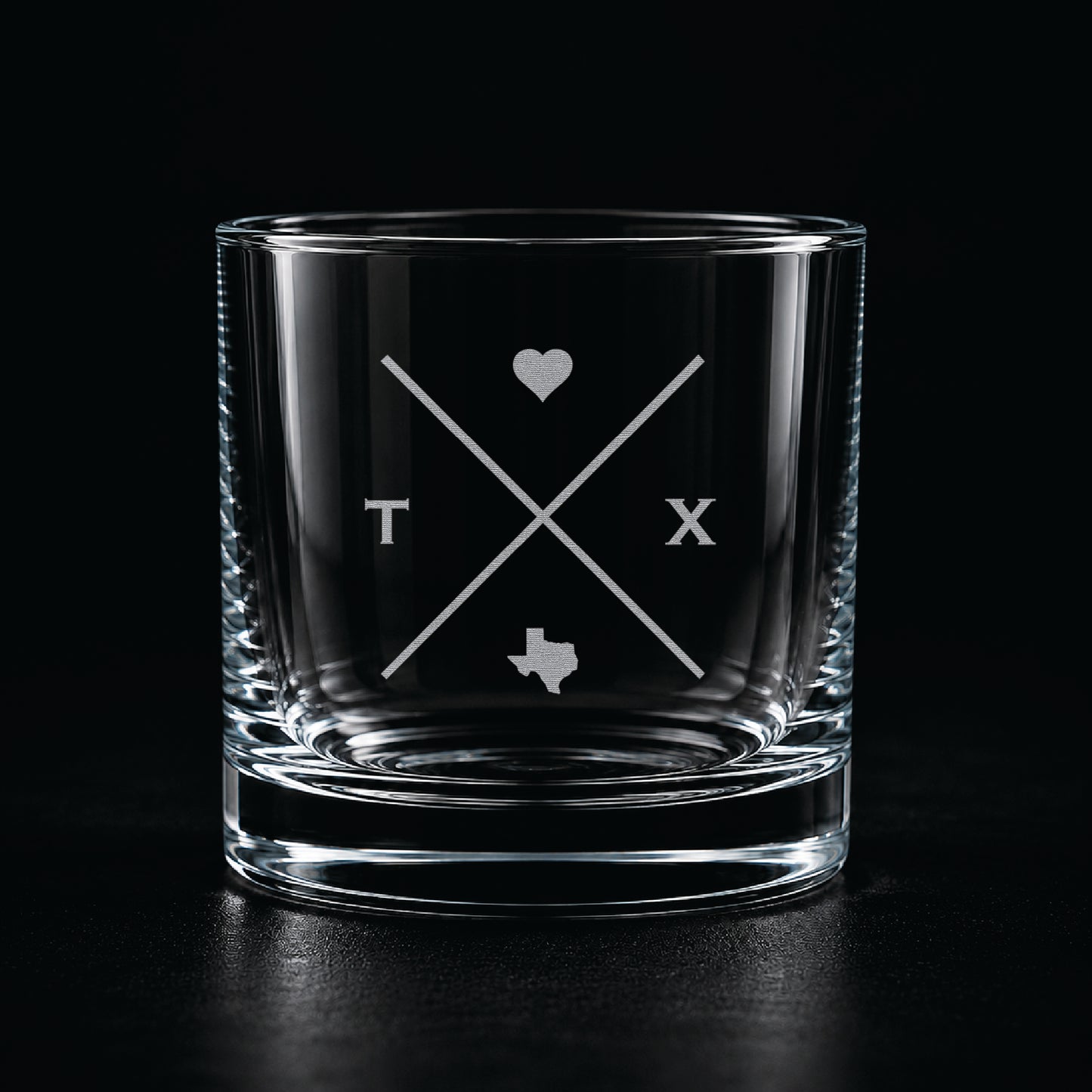 Modern etched rocks glass with minimalist Texas-inspired crossed line design on a dark moody background.
