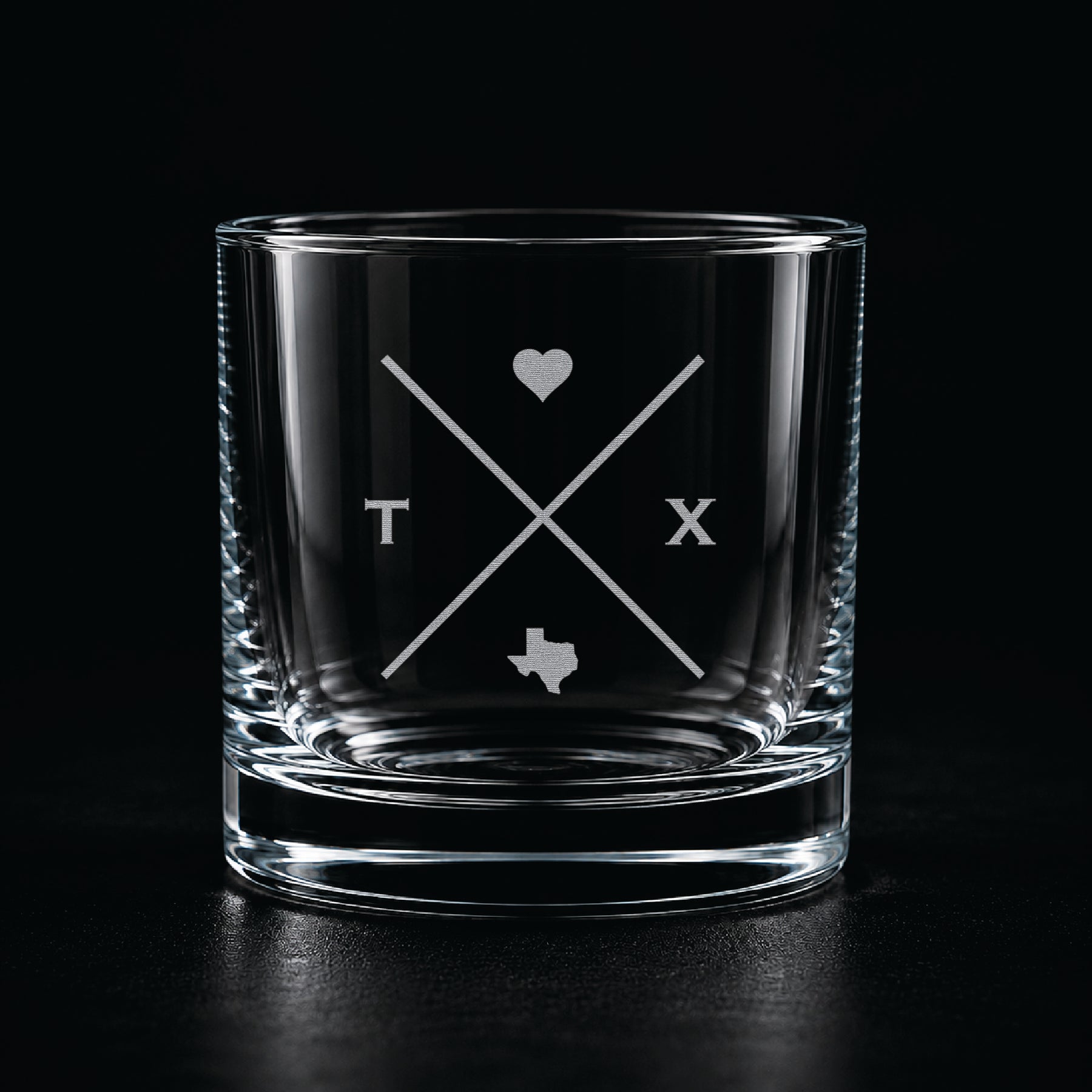 Modern etched rocks glass with minimalist Texas-inspired crossed line design on a dark moody background.