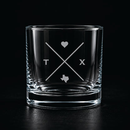 Modern etched rocks glass with minimalist Texas-inspired crossed line design on a dark moody background.