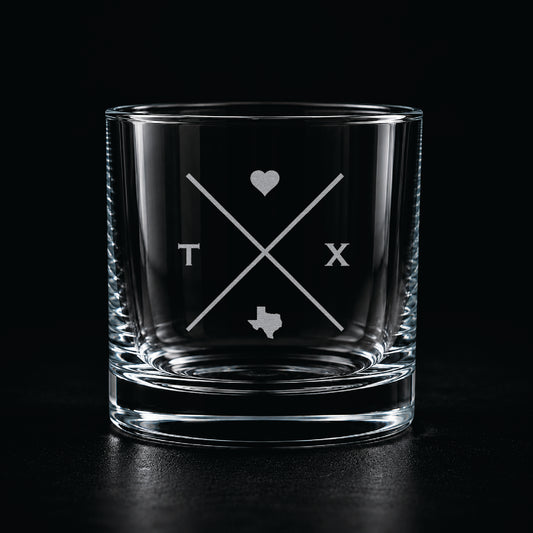 Modern etched rocks glass with minimalist Texas-inspired crossed line design on a dark moody background.