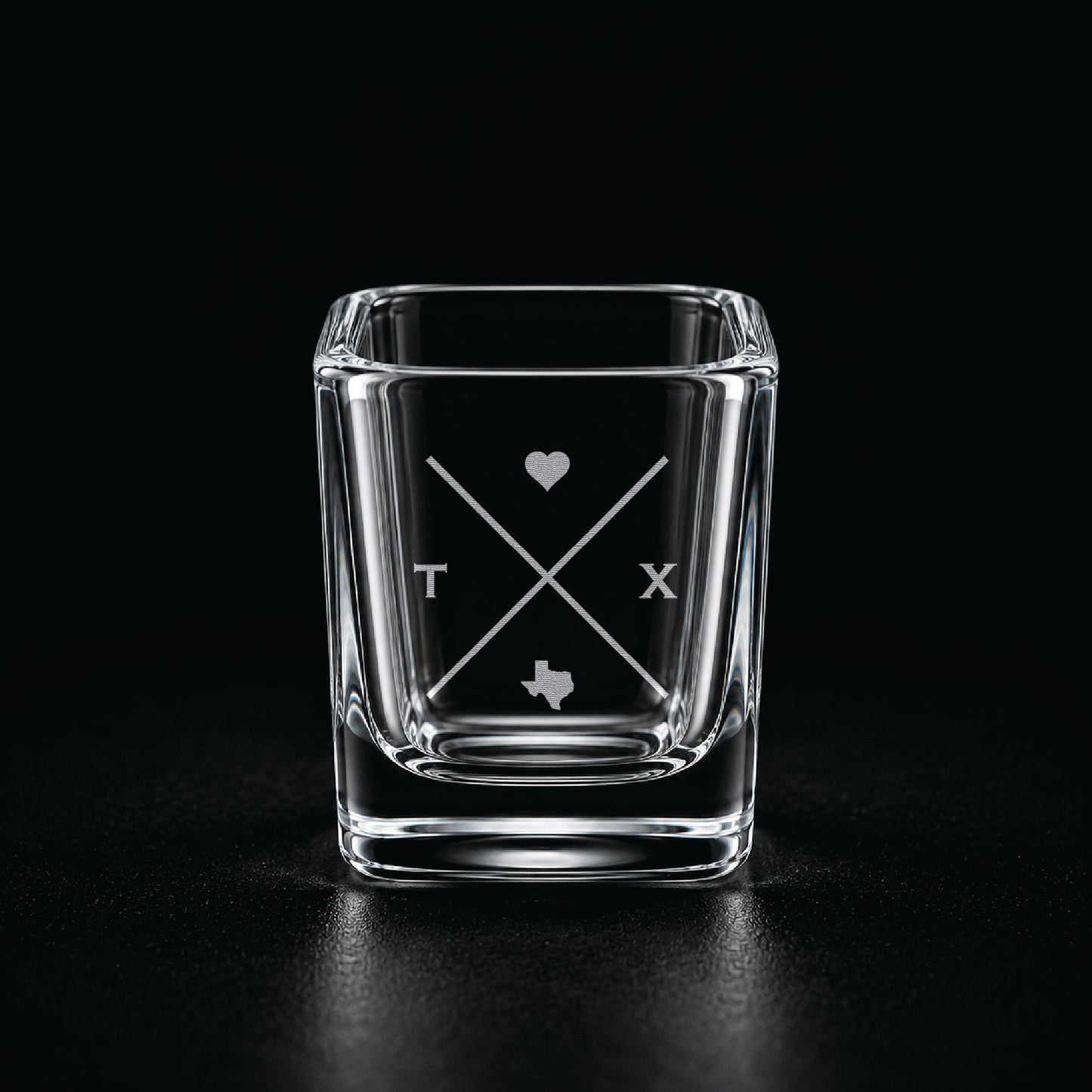Engraved Texas shot glass with modern crossed-line state design and frosted laser engraving on a dark background.