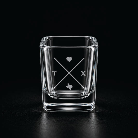 Engraved Texas shot glass with modern crossed-line state design and frosted laser engraving on a dark background.