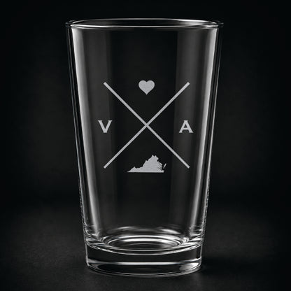Engraved Virginia pint glass featuring a minimalist crossed-line design with heart detail and Virginia silhouette on a dark background.