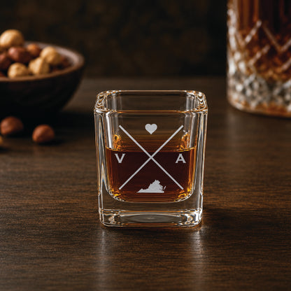 Engraved Virginia shot glass filled with whiskey in a warm bar-style setting, featuring a minimalist crossed-line design with heart detail and Virginia silhouette.