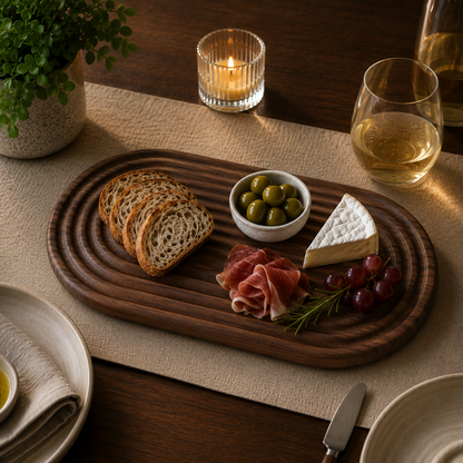 Walnut wood fluted charcuterie board styled with bread, olives, brie, grapes, and prosciutto in a moody dining table setting.