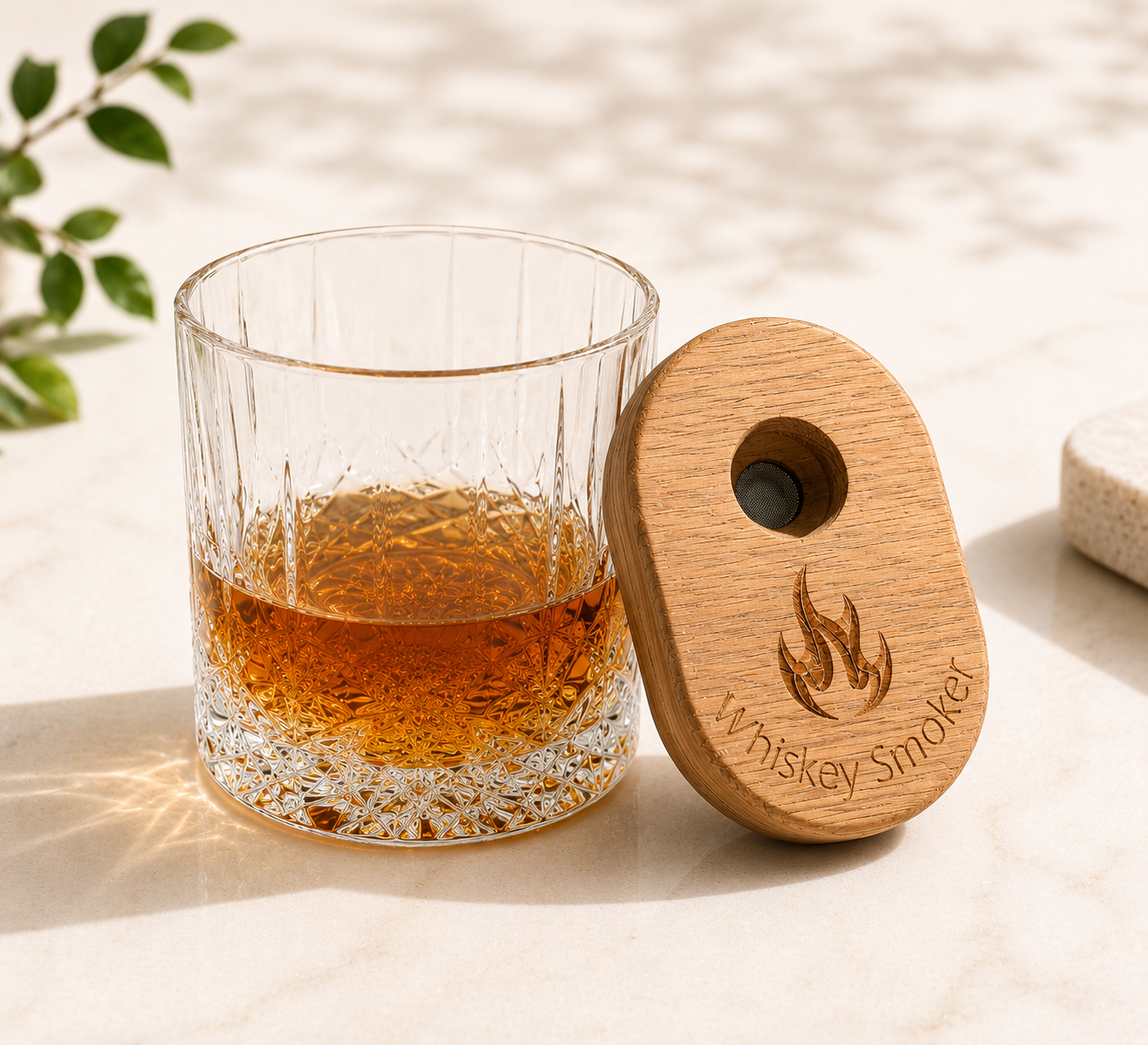 White Oak whiskey smoker leaning against a crystal bourbon glass filled with amber whiskey on a light neutral background. Features engraved flame design and rich wood grain detail in a refined, modern product styling scene.