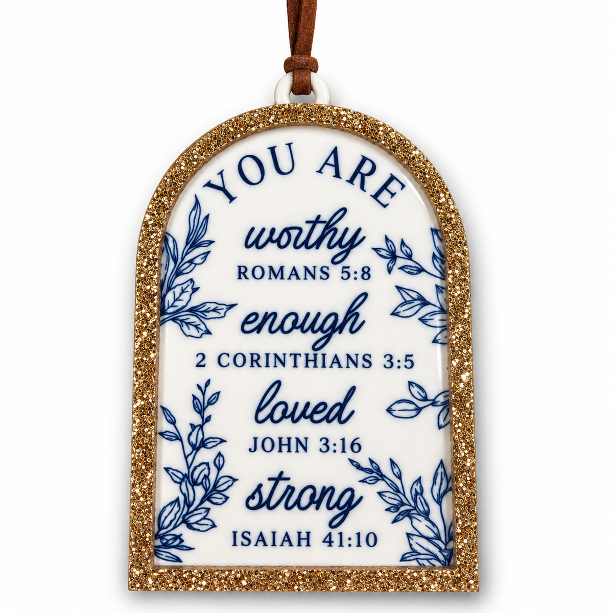 An arched Christmas ornament with a white center, blue script Bible verse text, blue botanical illustrations, and a glittery gold border, hanging from a brown ribbon on a white background.