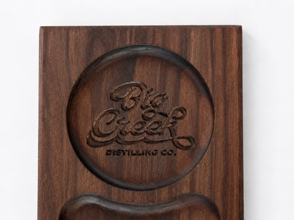 Close-up of walnut cigar tray with recessed drink well engraved with “Big Creek Distilling Co.” and a carved pocket below.