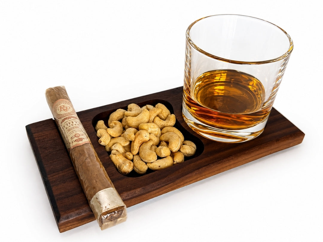 Walnut cigar tray holding a cigar, cashews, and a rocks glass filled with whiskey in the recessed drink holder.