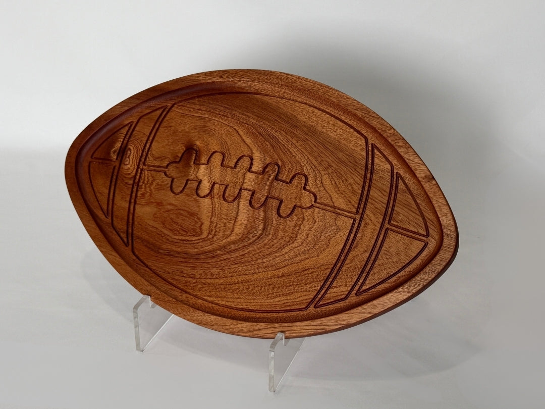 Football-shaped wooden serving tray with a fully recessed center and carved rim detail, displayed on a white background with visible wood grain and engraved football stitching design.